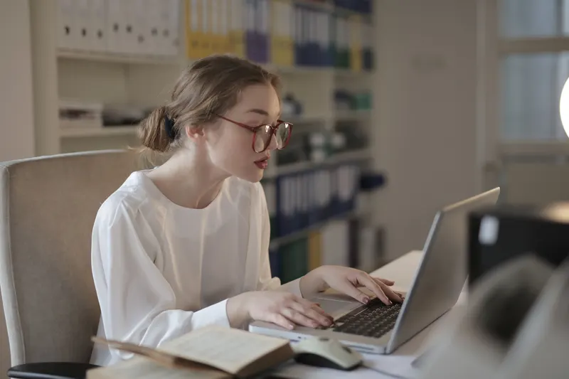 Administratief medewerker werkt op een laptop aan een bureau, met ordners op de achtergrond