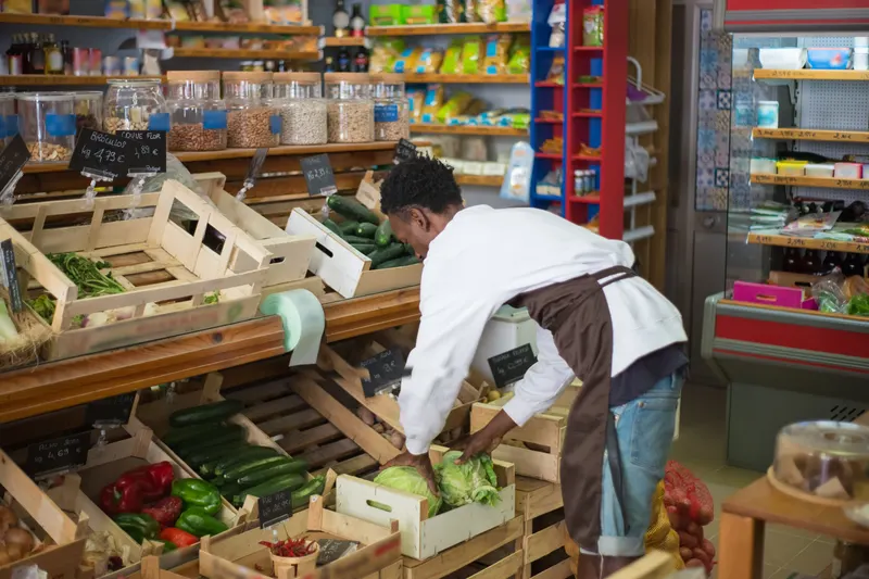 Winkelmedewerker met schort vult houten kratten met groente in een kleine supermarkt