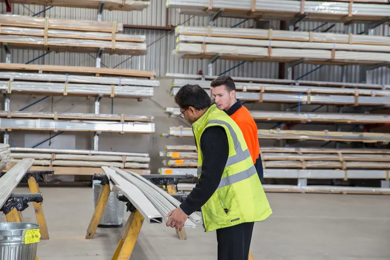 Medewerker in veiligheidshesje laat een collega materiaal zien in een opslaghal