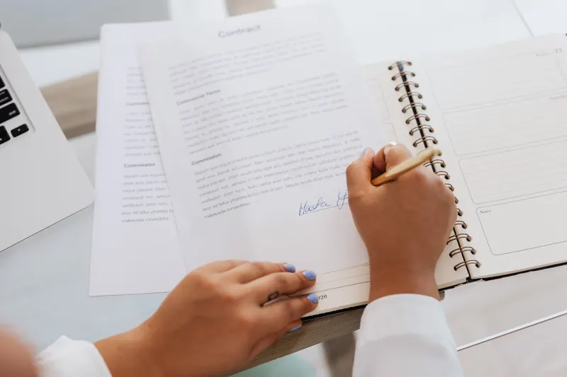 Hand zet een handtekening onder een contract op een bureau