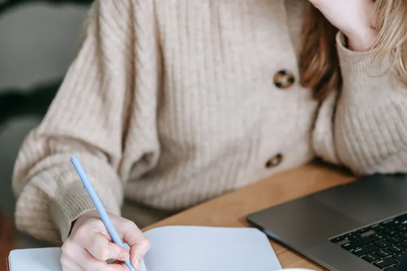 Vrouw schrijft notities in een schrift bij haar laptop om zich voor te bereiden op het gesprek