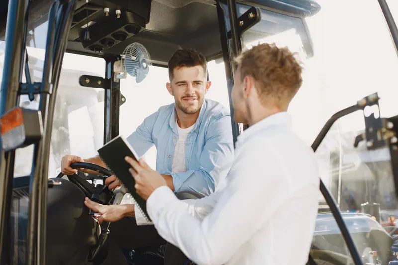 Instructeur met notitieboek geeft uitleg aan een bestuurder achter het stuur van een heftruck