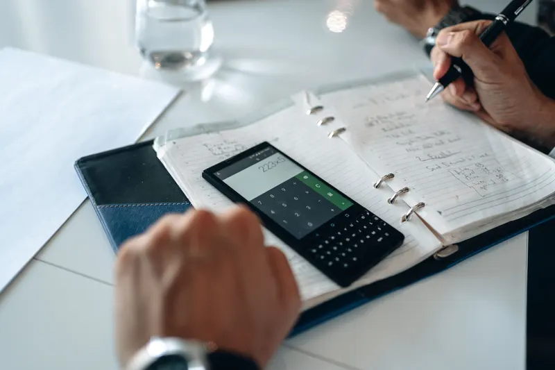Handen rekenen kosten uit met de rekenmachine op een telefoon en noteren de bedragen in een agenda