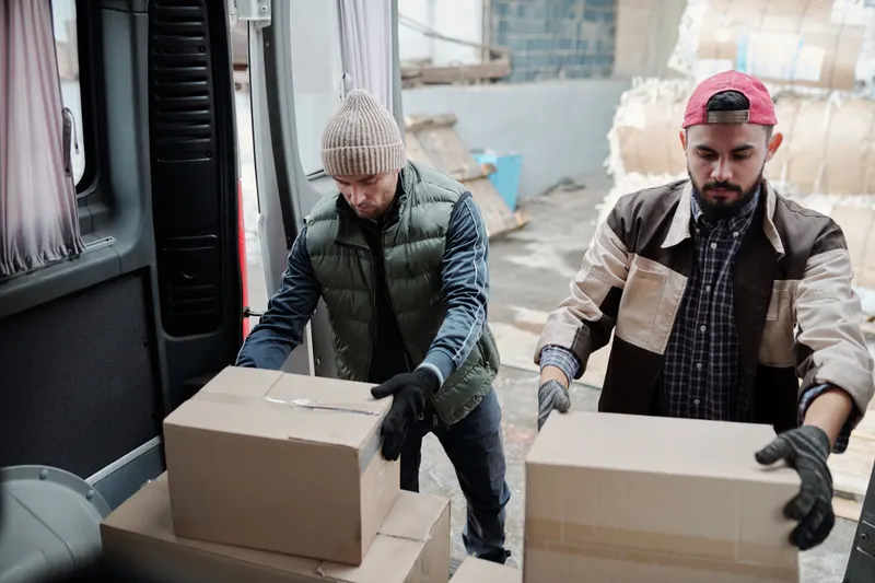 Twee logistiek medewerkers laden kartonnen dozen in een bestelbus