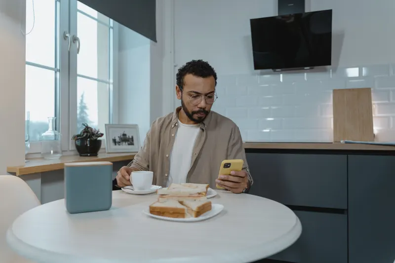 Man aan de keukentafel bekijkt zijn loonstrook op zijn telefoon