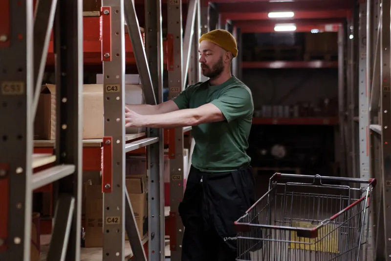 Orderpicker met winkelwagen pakt producten uit een stelling in een magazijn
