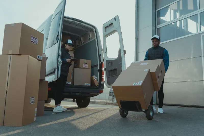 Logistiek medewerkers laden dozen met een steekwagen in een bestelbus bij een bedrijfshal