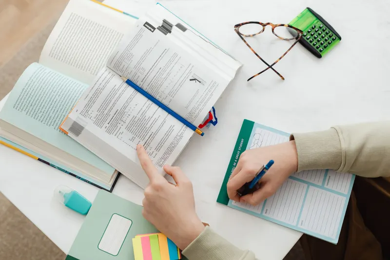 Studieboek, rekenmachine en een planning op tafel terwijl iemand werk en studie inroostert