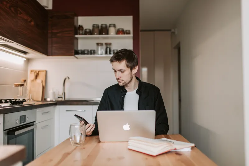 Man zoekt aan de keukentafel met laptop en telefoon naar nieuw werk