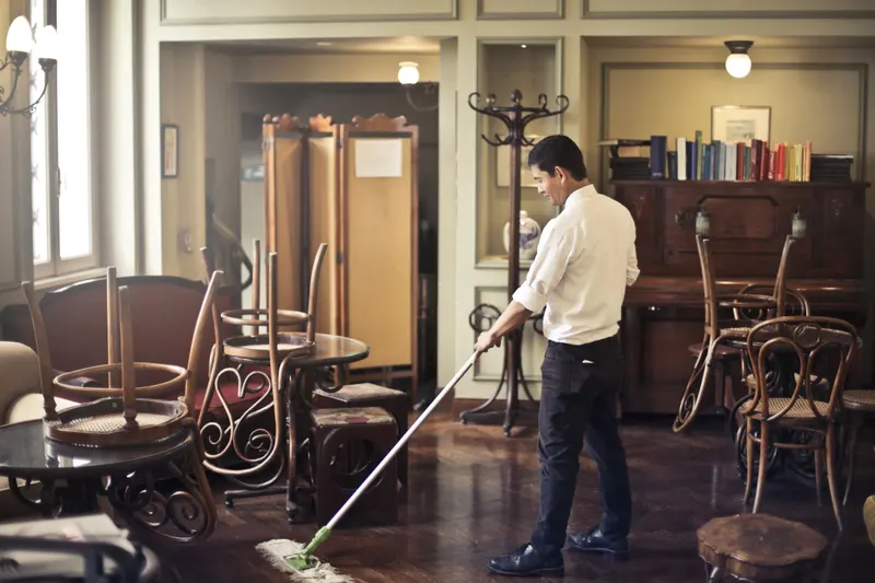 Schoonmaker dweilt de houten vloer van een café met de stoelen op tafel