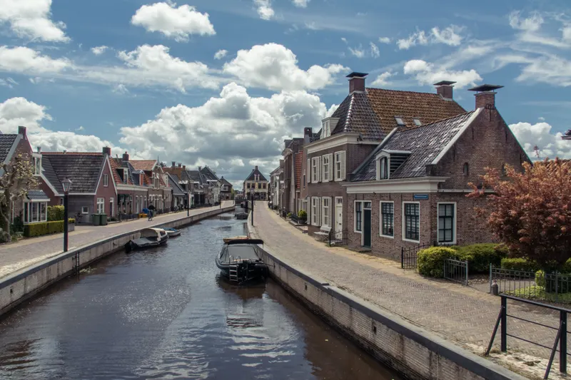 Vaart met bakstenen huizen en bootjes in het Friese dorp Kollum onder een wolkenlucht