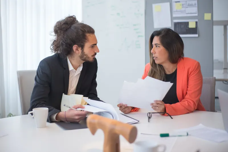 Werkgever en adviseur bespreken papieren aan tafel om te kiezen hoe ze personeel werven