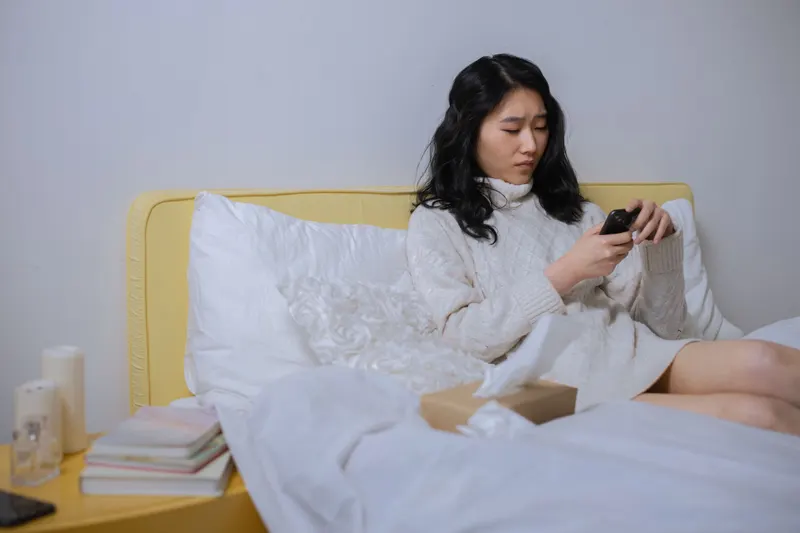 Zieke vrouw zit in bed met haar telefoon in de hand om zich ziek te melden